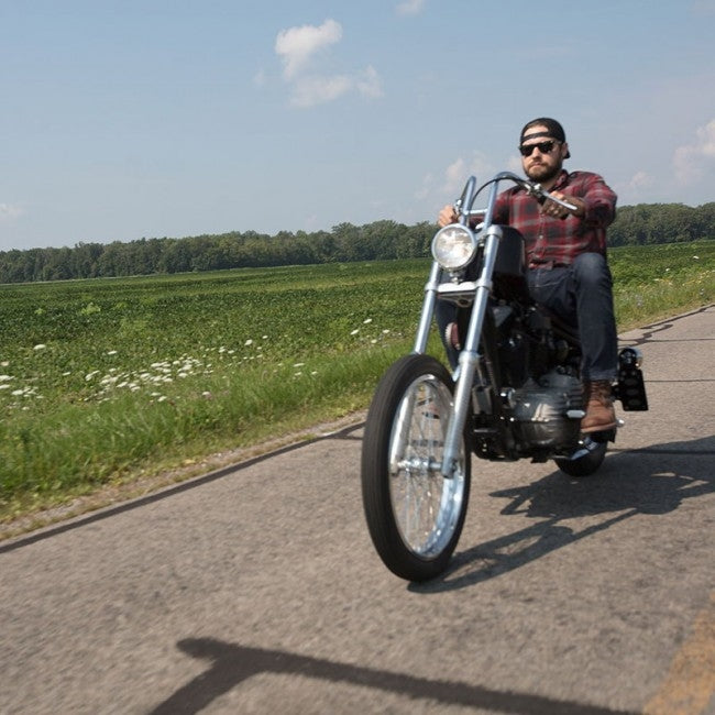 A man cruising on a TC Bros. chrome motorcycle down a country road.