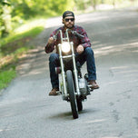 A man riding a TC Bros. motorcycle down a country road with TC Bros. 1" Rabbit Handlebars - Chrome gleaming in the sunlight.