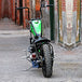 A versatile TC Bros. LED Black 33 Ford Replica Side Mount Tail Light/License Plate Bracket is attached to a green motorcycle parked on a street.