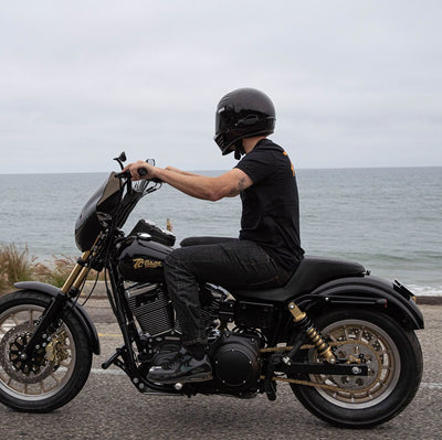 A man riding a black motorcycle near the ocean with a TC Bros. Laydown License Plate Mount for Harley Davidson.