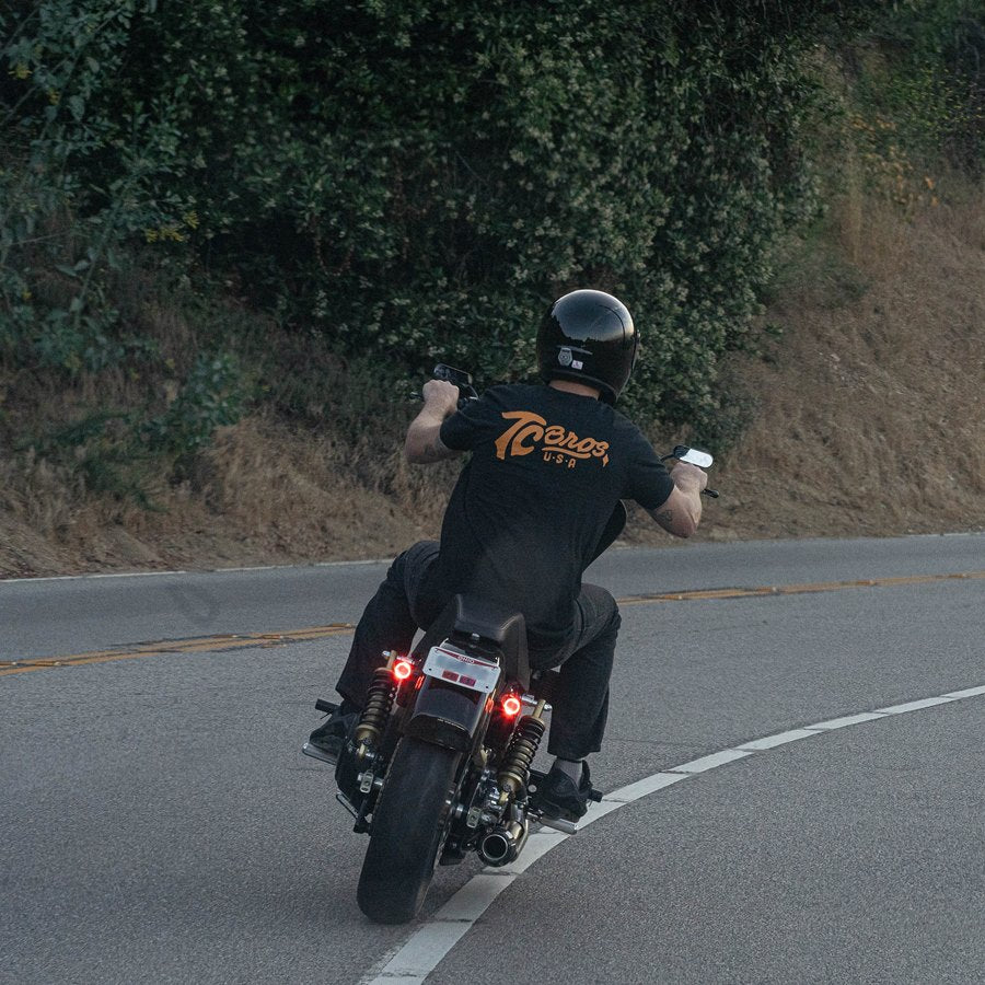 A man riding a motorcycle down a road with a TC Bros. Laydown License Plate Mount for Harley Davidson.