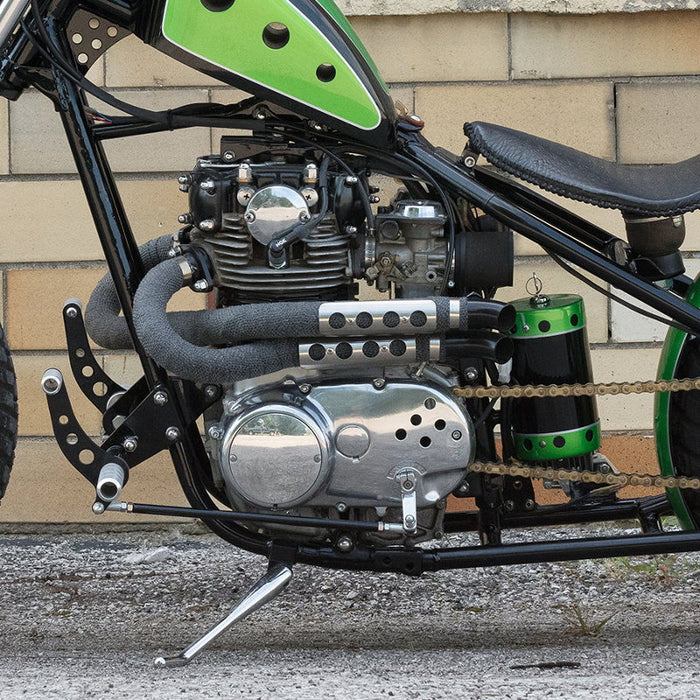 A TC Bros. green motorcycle parked in front of a brick wall.