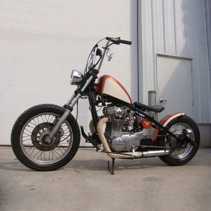 A TC Bros. motorcycle parked in front of a garage, showcasing its powerful engine and distinct TC Bros. exhausts.