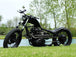 A motorcycle parked in the grass near a lake with a black custom Yamaha XS650 "Ya Mama" Exhaust System By Pandemonium (Fits 1974-1982 XS650).