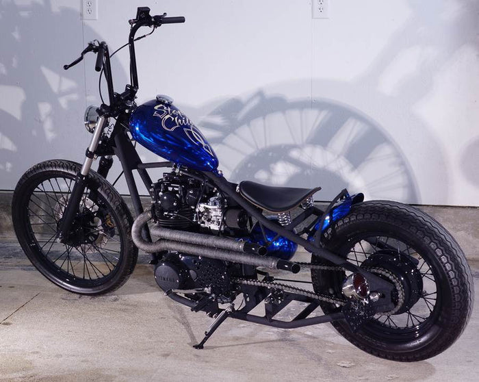 A custom blue and black Yamaha XS650 motorcycle parked in a garage, equipped with the Pandemonium "Ya Mama" Exhaust System.