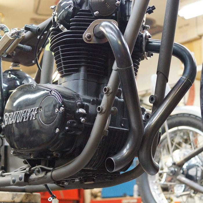 A black Yamaha XS650 "Double D" Exhaust System by Pandemonium motorcycle is sitting in a garage.
