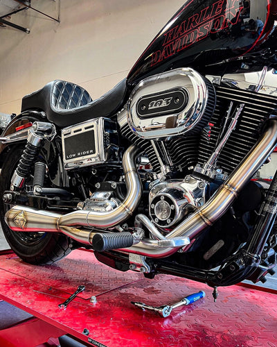 A SP Concepts Big Bore Exhaust 06-17 Dyna (stainless) is being worked on in a garage, focusing on enhancing its performance by installing a stainless steel exhaust.