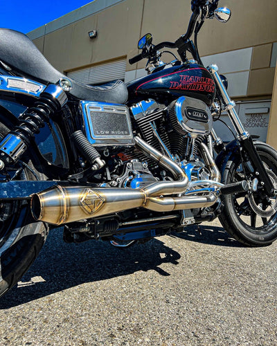 A motorcycle with an SP Concepts Big Bore Exhaust 06-17 Dyna (stainless) is parked in front of a building.
