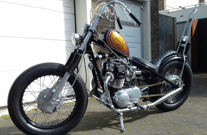 A TC Bros. Tall Kickback DIY Sissy Bar Kit motorcycle parked in front of a garage.