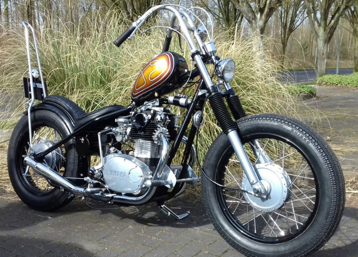 A black motorcycle parked in front of a grassy area with a TC Bros. Tall Kickback DIY Sissy Bar Kit.