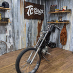 A TC Bros. motorcycle with a wooden floor parked in a room alongside the TC Bros. Extra Narrow Triple Tree Set for 2004-2007 Harley Davidson Sportster and CNC machined parts.