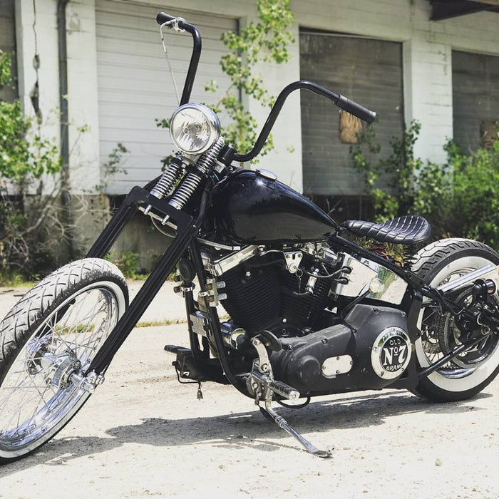 A black motorcycle with TC Bros. 1" Springer Apes Handlebars - 12" Black parked in front of a building.