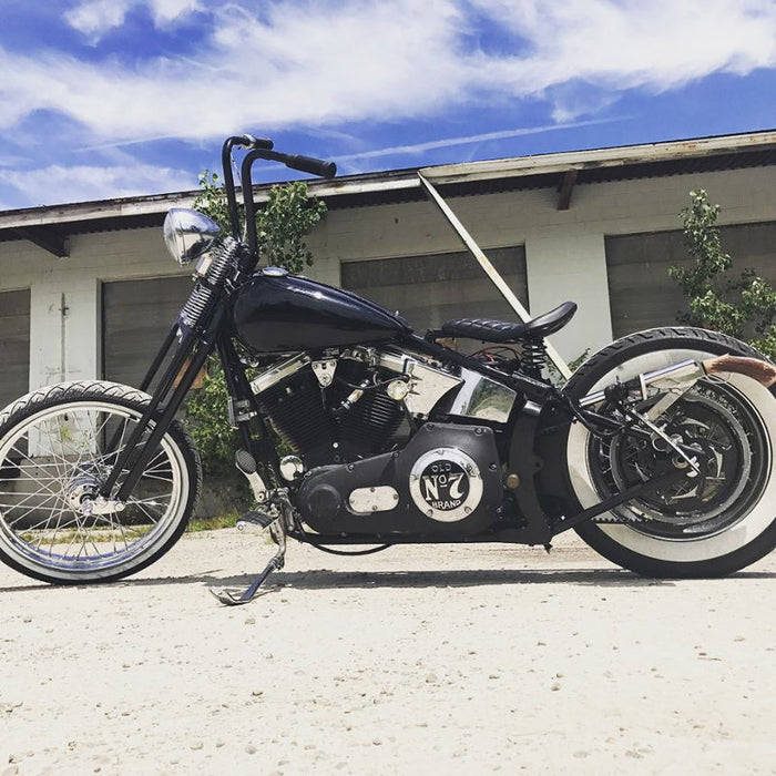 A black and white motorcycle with TC Bros. 1" Springer Apes Handlebars - 12" Chrome handlebars parked in front of a building.