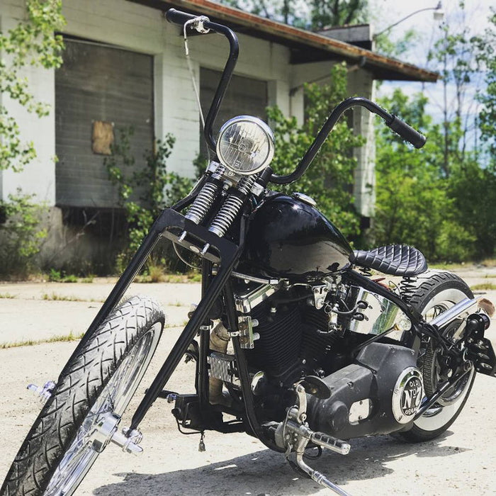 A black motorcycle, equipped with TC Bros. 1" Springer Apes Handlebars - 12" Black, parked in front of a building.