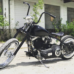 A black motorcycle with TC Bros. 1" Springer Apes Handlebars - 12" Chrome parked in front of a building.
