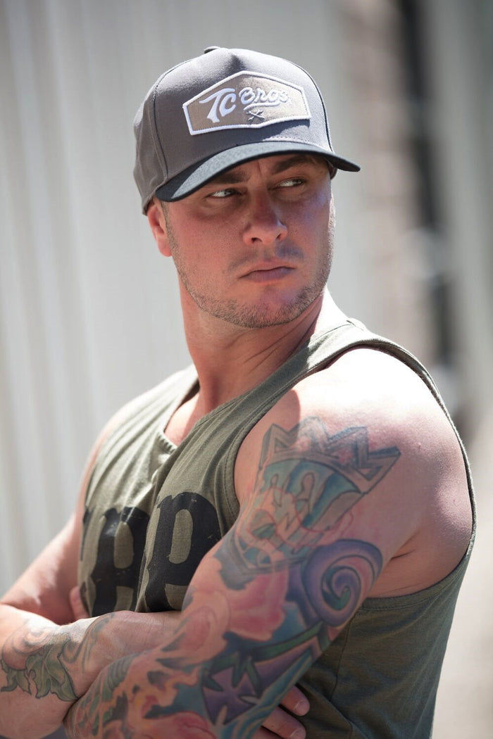 A man with tattoos and a TC Bros. Shield Snapback Hat - Charcoal/Black.