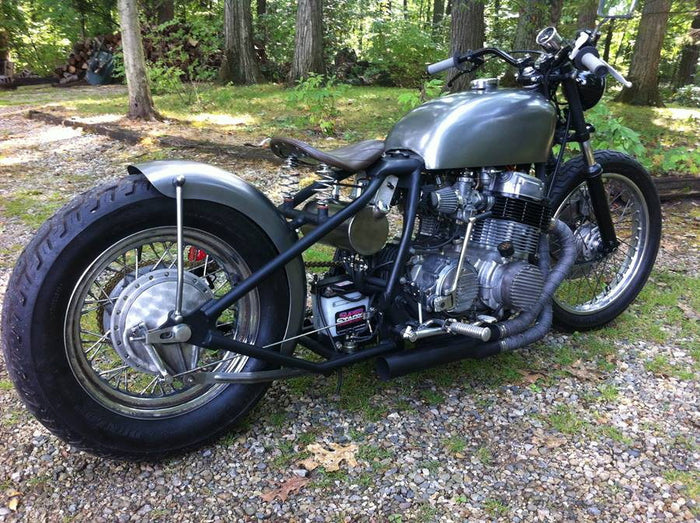 A TC Bros. Honda CB750 Weld On Hardtail Frame motorcycle parked in the woods.