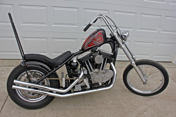 A black and red TC Bros. motorcycle with Sportster weld-on hardtails parked in front of a garage, equipped with the TC Bros. Hardtail Rigid Cobra Seat Black Diamond.