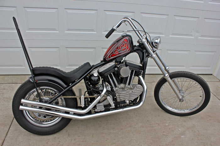 A black and red TC Bros. Hardtail Rigid Cobra Seat Black Pleated motorcycle parked in front of a garage.