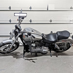 The TC Bros. Front Crash Bar for 1991-2017 Harley-Davidson Dyna is a black metal engine guard bracket with side mounts, bolts, washers, and extra metal pieces—perfect as a front crash bar for your Dyna motorcycle.