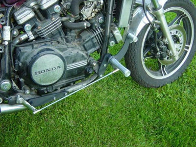 The engine of a TC Bros. Honda Magna V45 Forward Controls Kit motorcycle is parked on the grass.