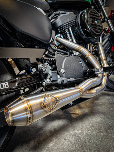 An SP Concepts Lane Splitter Exhaust Sportster 2014-2022 (stainless) motorcycle is parked in a garage.