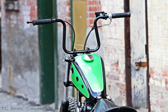 A vintage bike with Moto Iron® Vintage Style 7/8" Diameter Black Grips parked in front of a brick building.