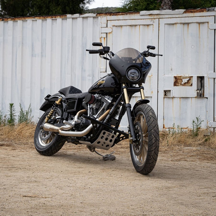 A TC Bros. motorcycle parked in front of a shed, equipped with TC Bros. Dyna Skid Plate 1991-2017 Models - Aluminum mounting hardware and a skid plate.