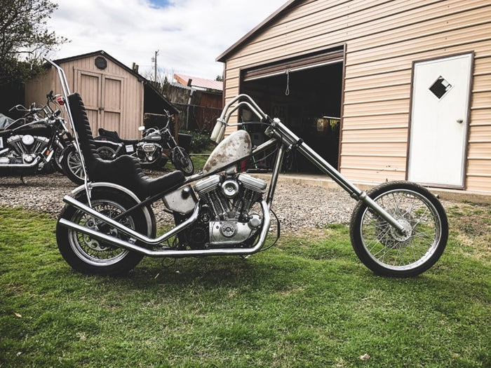 A TC Bros. King & Queen Hardtail Seat Black Pleated motorcycle parked in front of a garage.