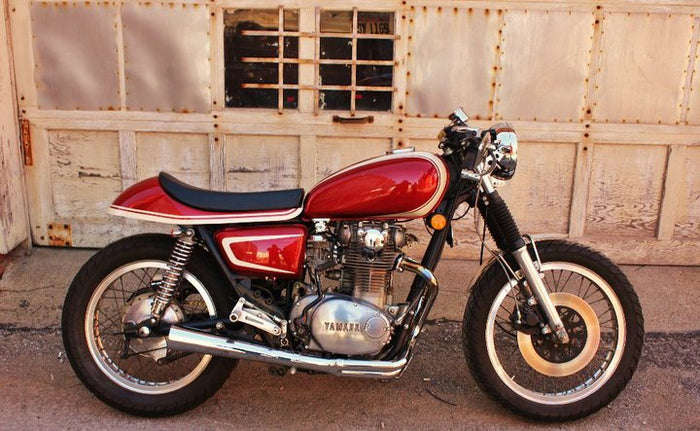 A red motorcycle parked in front of a garage with Loaded Gun Custom Universal Rearsets by TC Bros.