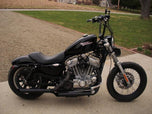 A black Burly Slammer 10.5" Shocks for Harley Davidson Sportster XL 1988-2003 motorcycle parked in front of a house.