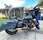 The SP Concepts Lane Splitter Exhaust for Harley Touring 2017-2025 – Stainless, with visible welds, sits on a workbench beside an American flag welding helmet—ready to upgrade your ride in style.
