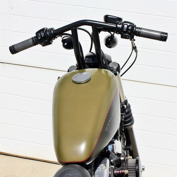 A green motorcycle with TC Bros. 1" Whiskey Handlebars - Black triple trees parked in front of a garage.